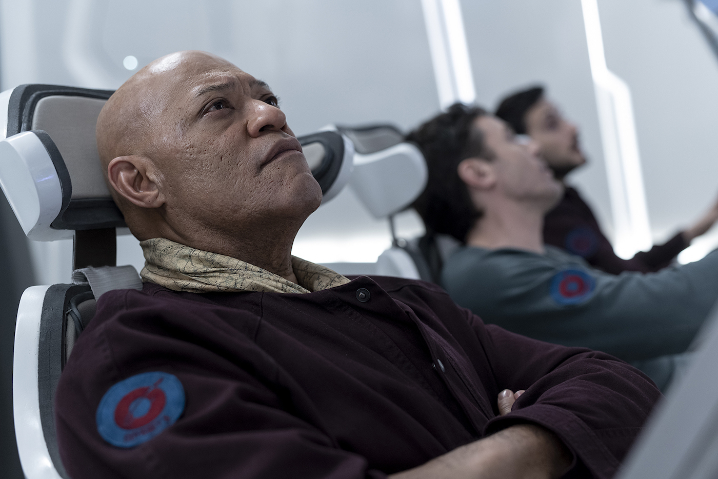A man looking at a screen with a concerned expression on his face. Two other men in the background.